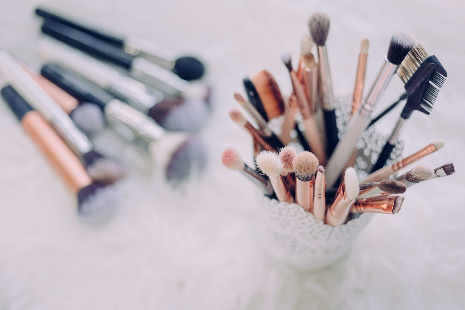 A dense collection of makeup brushes standing in a textured white holder beside scattered lip products
