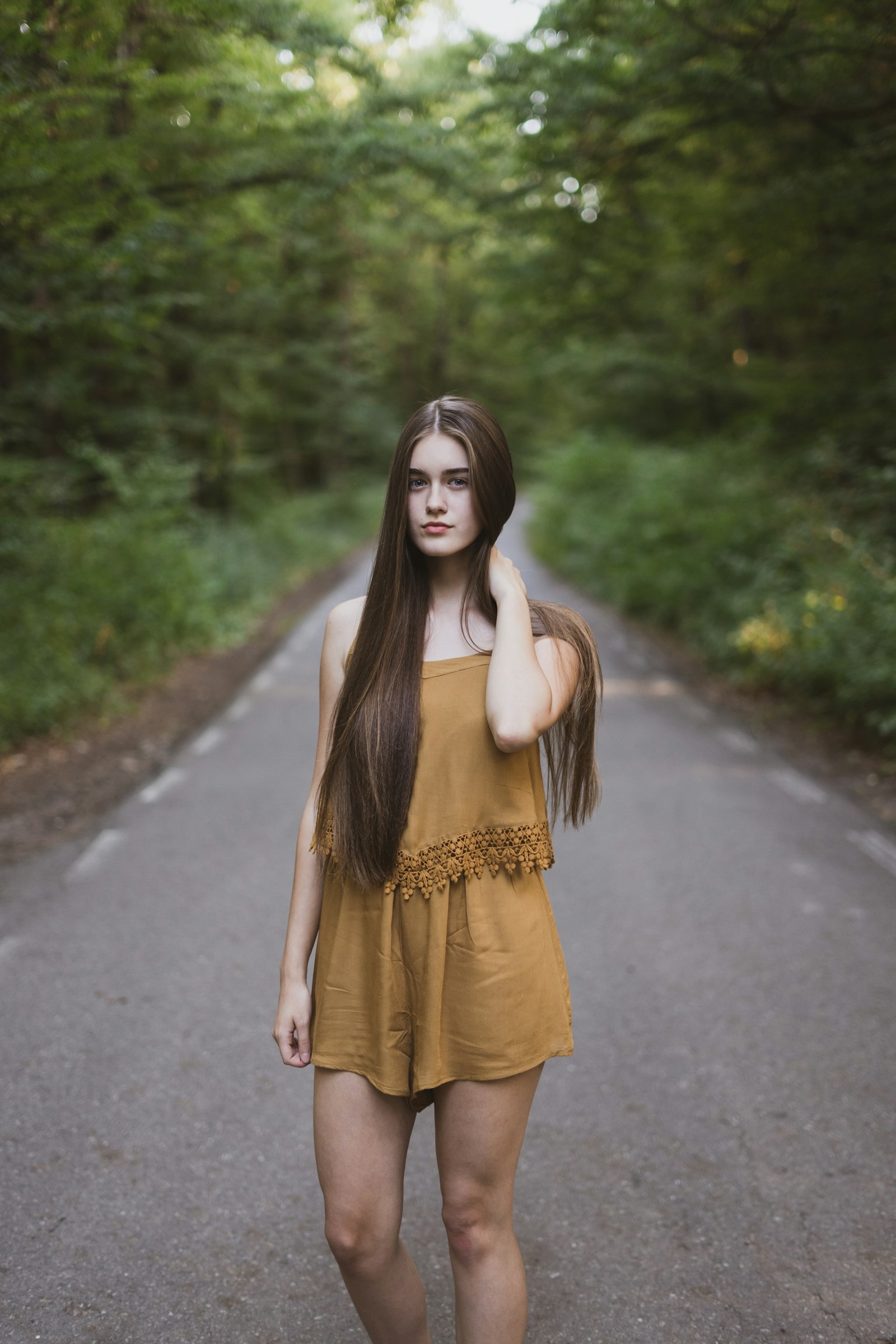 A woman with very long dark hair standing on an empty tree-lined road