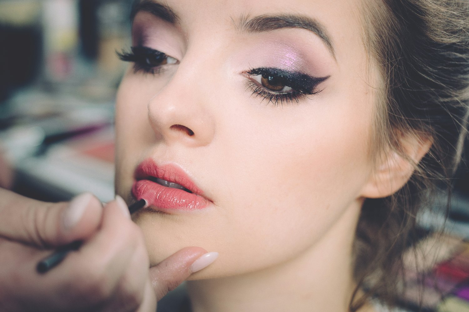 Close-up of a makeup artist applying lip colour to a model with dark eyeliner