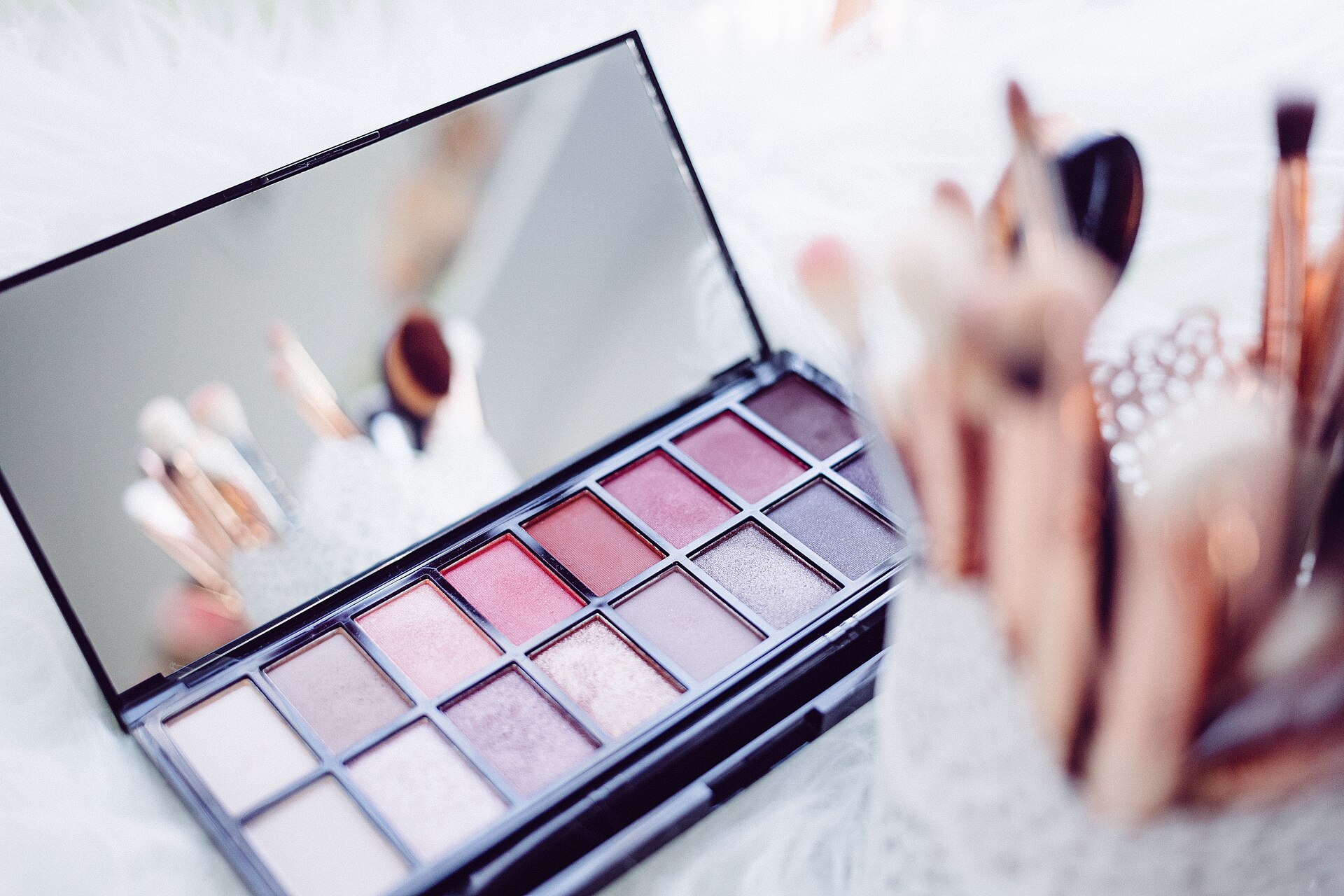 An open eyeshadow palette in rose tones with blurred makeup brushes in the foreground