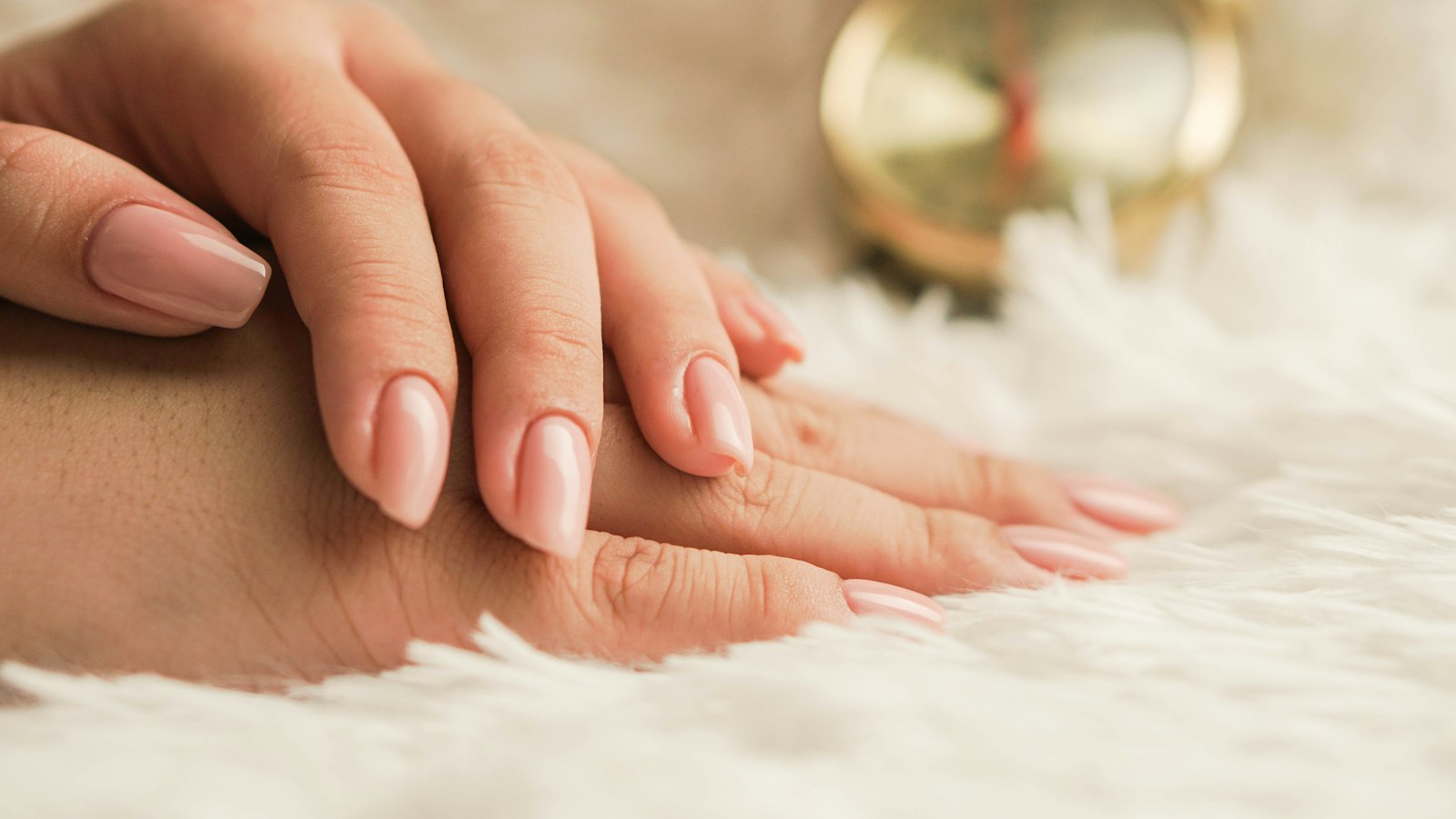 A hand with a glossy nude manicure resting on white faux fur