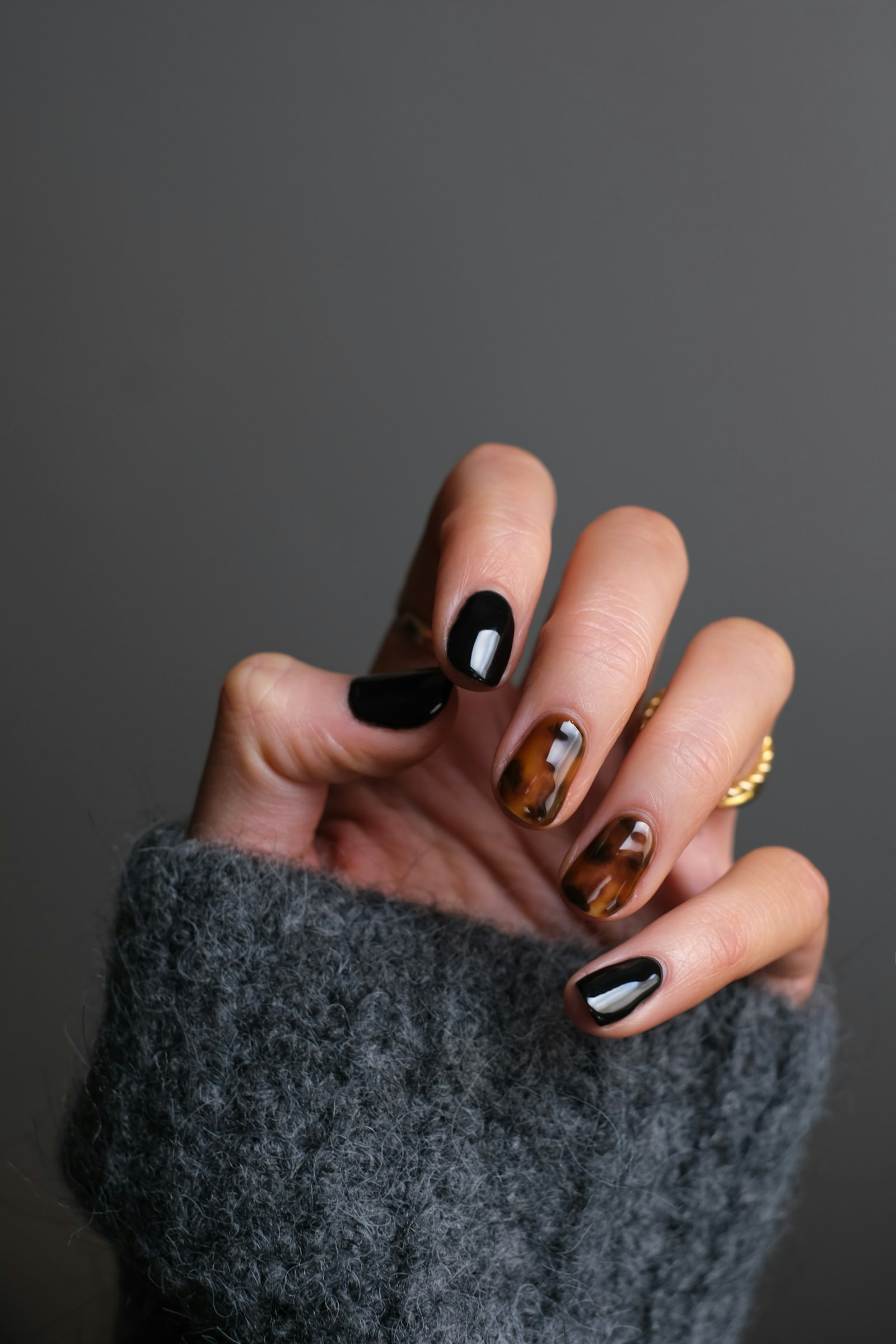 Close-up of a hand with glossy black and tortoiseshell nails against a grey sweater cuff