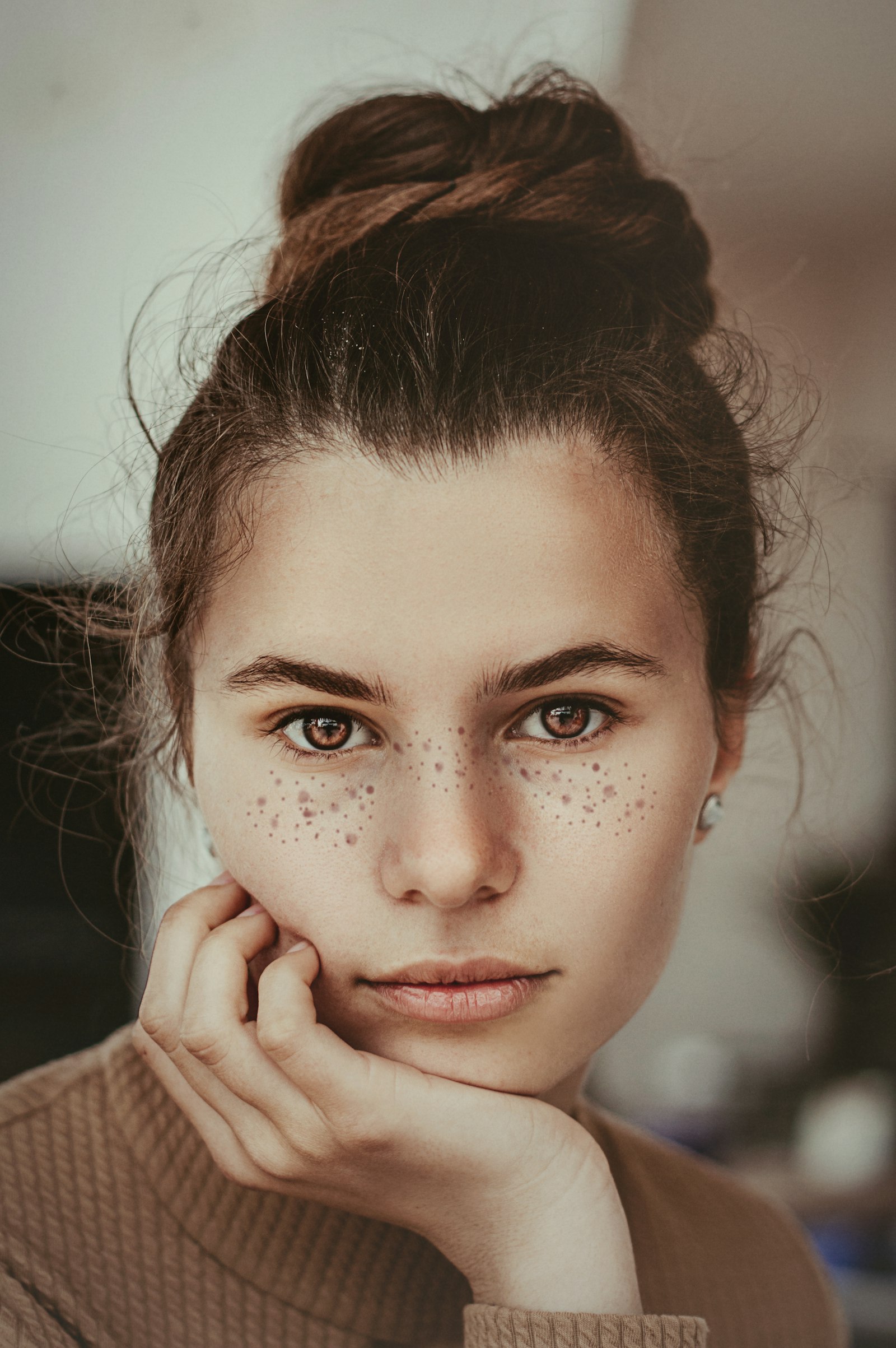 A close portrait of a young woman with freckles and brown eyes resting her chin on her hand